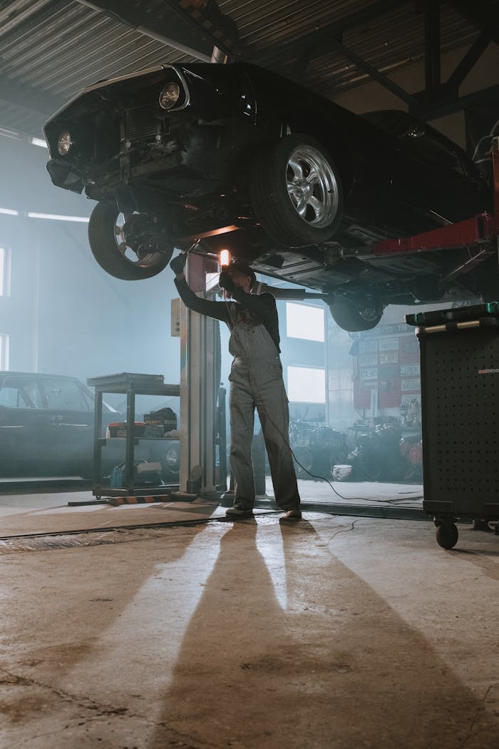 Mechanic performing maintenance on elevated car in dimly lit garage, showcasing automotive repair work.